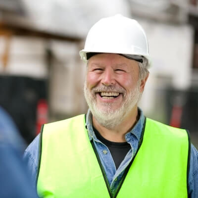 Man wearing white work helmet and reflective vest smiling at camera.